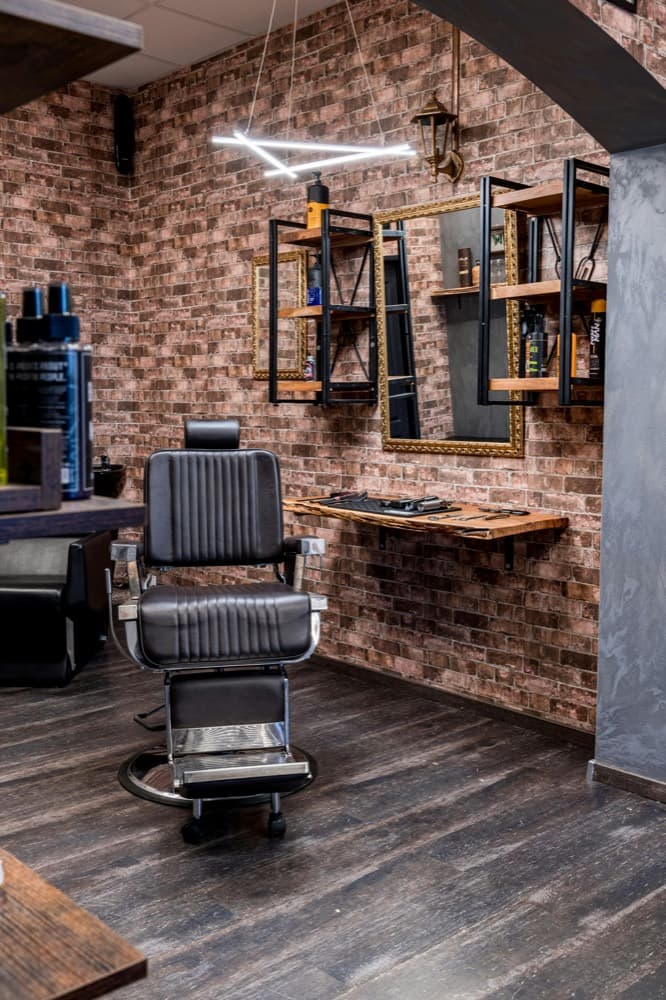 A barber chair against a brick wall with tools laid out on a shelf